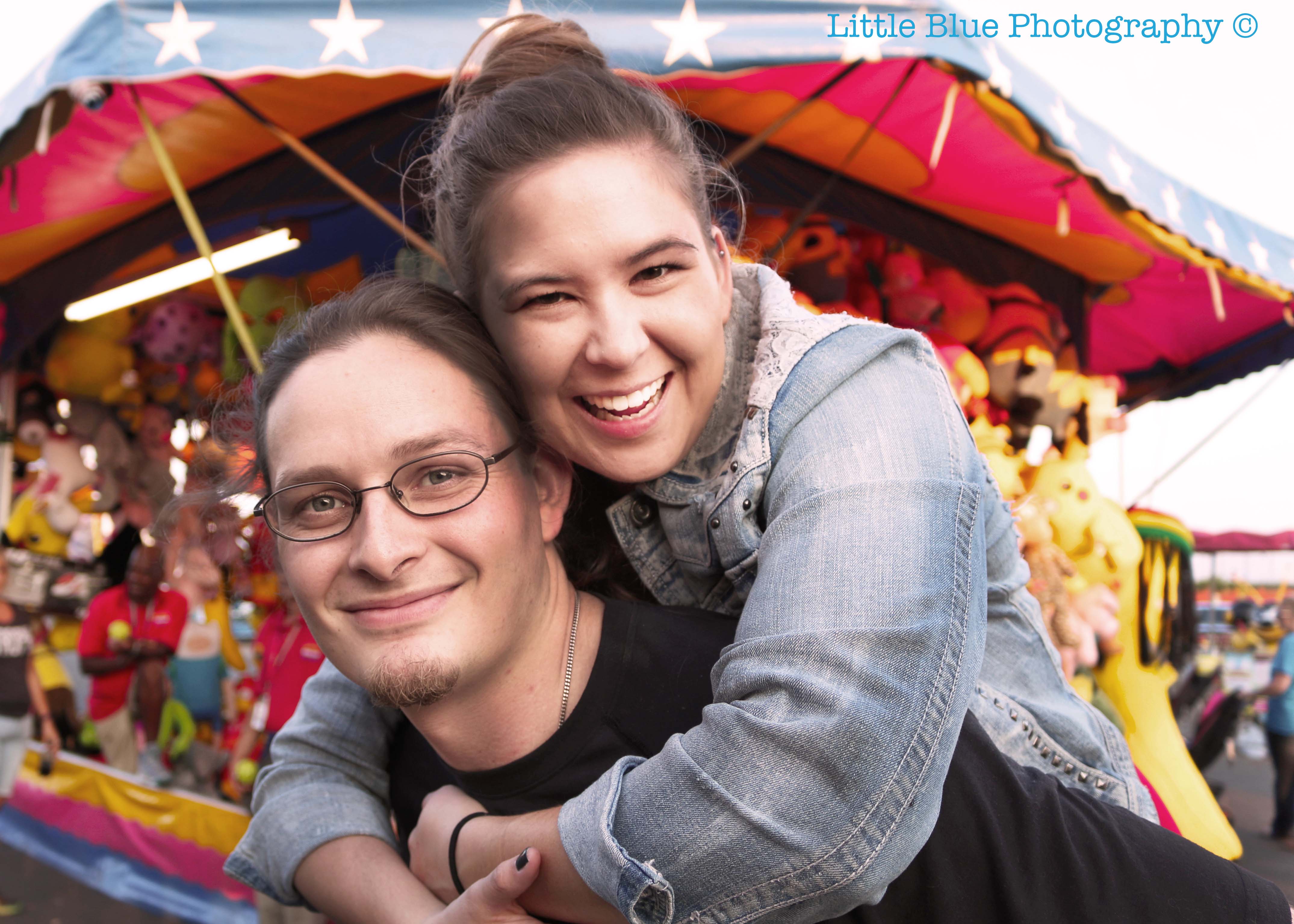 Image of man giving a woman a piggy back ride in front of a carnival game.