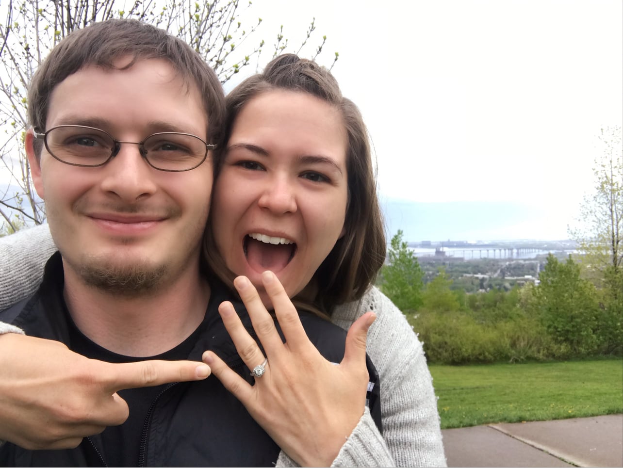 Man and woman smiling. Woman pointing to engagement ring on her finger.